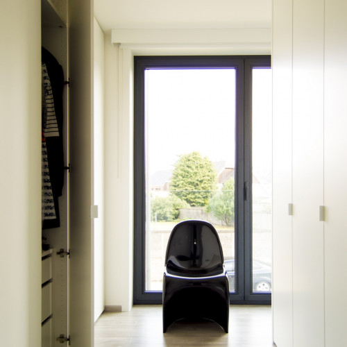 In de ruime slaapkamer ontworpen we een inloopdressing waardoor de slaapkamer iets kleiner en gezelliger lijkt. Om het slaapgedeelte duidelijk te scheiden van de dressing creërden we als het ware een scheidingswanden door de kasten kamerhoog te maken.  Aan de kant van het slaapgedeelte zorgt de smallere kastenwand voor een mooie doorgang en komt hierdoor nog zoveel mogelijk natuurlijk daglicht binnen.  Rondom de maatkast plaatsten we een MDF-wand zodat het lijkt alsof de kast in een daarvoor voorziene nis in de kamer geïntegreerd wordt.  Voor de draaideuren koos de familie voor wit gelakte L-grepen.  Kast-ID Asse